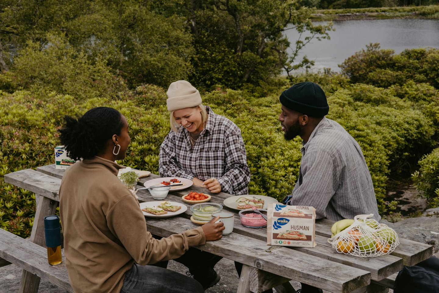Three friends laugh together while eating at an outdoor table.